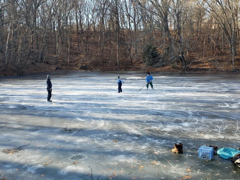 photo of 3 children playing hockey on a frozen pond