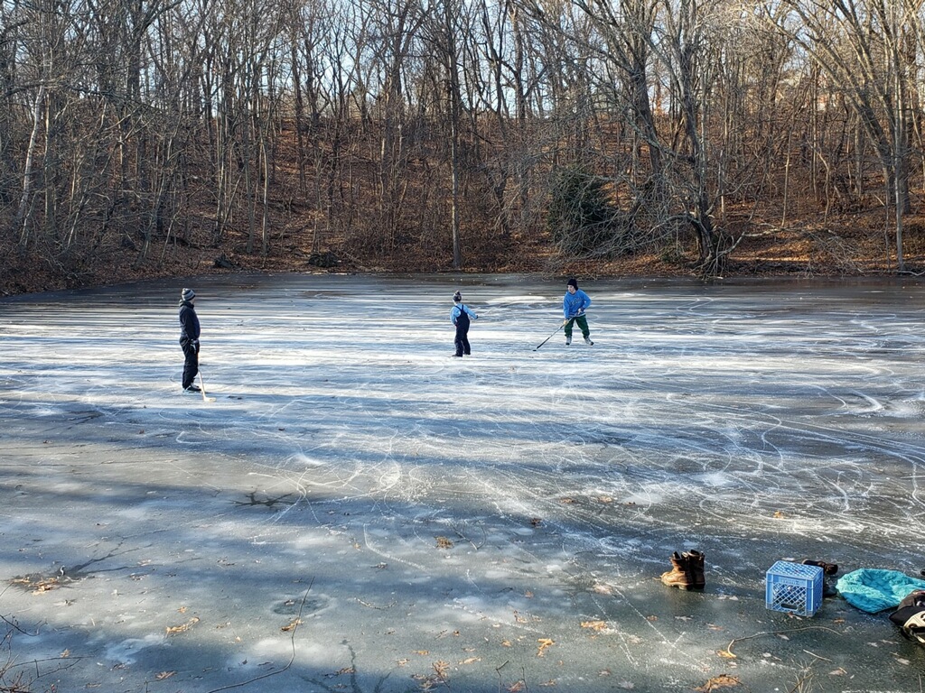 photo of 3 children playing hockey on a frozen pond