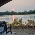 Photo of the sun shining over a park bench that is facing towards the water