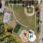 an birds-eye-view photo of a baseball field, turf sports field, basketball court, playground structures and splashpad areas