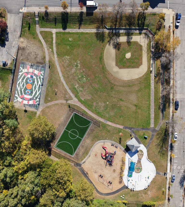 an birds-eye-view photo of a baseball field, turf sports field, basketball court, playground structures and splashpad areas
