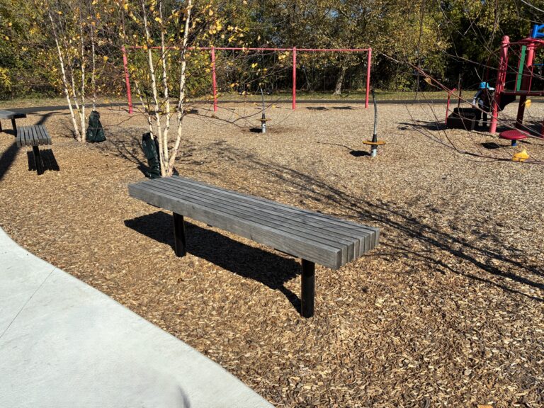 photo showing a park bench with a swingset in the background