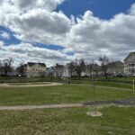 photo showing a baseball field with trees and houses in the background