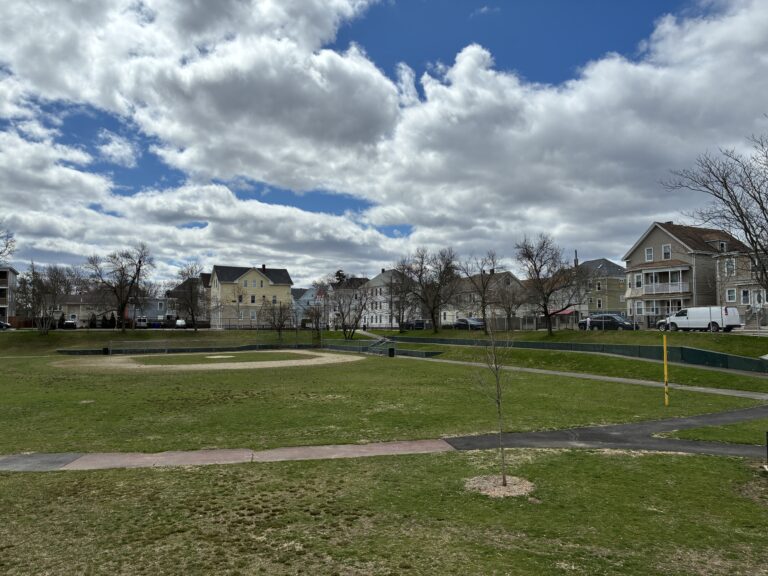 photo showing a baseball field with trees and houses in the background