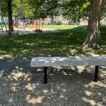 photo of a park bench with playground structures and trees in the background