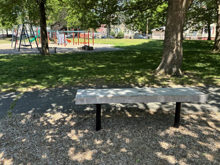 photo of a park bench with playground structures and trees in the background