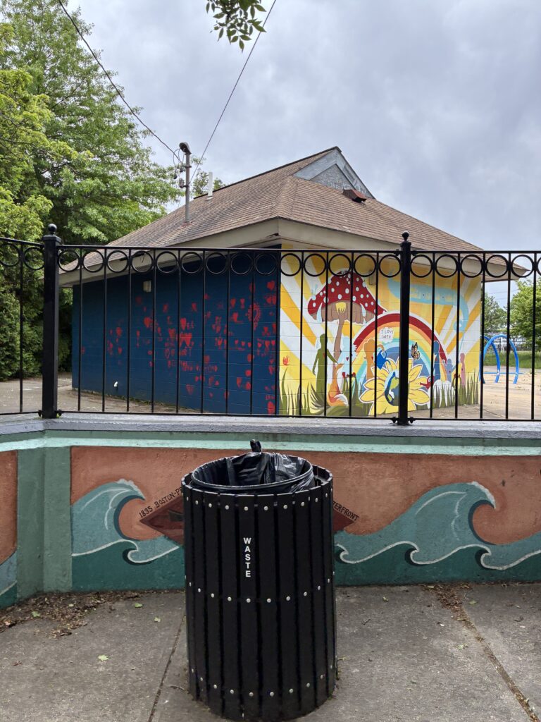 a photo showing a trash can and a wall painted with waves and a building with a bright mural painted on the side