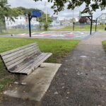 photo showing a park bench with a basketball court in the background