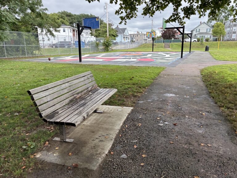 photo showing a park bench with a basketball court in the background