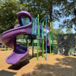 Merino Park play structure for ages 5-12 features a climbing tube, spiral slide, fire pole, and rock wall