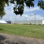 photo showing a sports field and net with wind turbines in the background