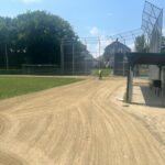 photo showing baseball field with someone raking the dirt areas