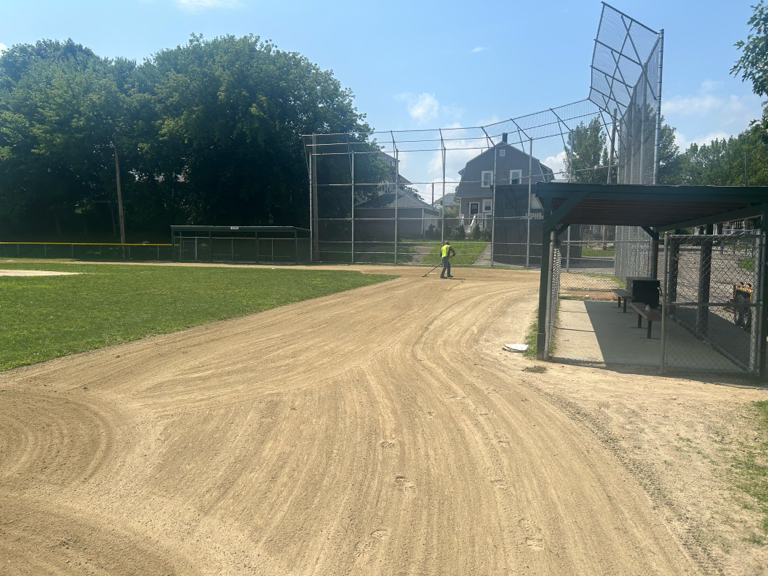 photo showing baseball field with someone raking the dirt areas