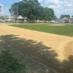 photo showing baseball field with someone raking the dirt areas