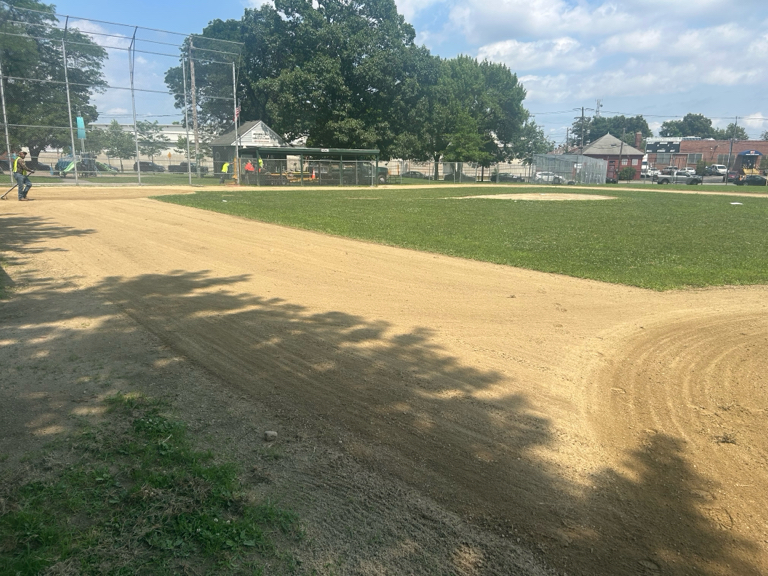 photo showing baseball field with someone raking the dirt areas