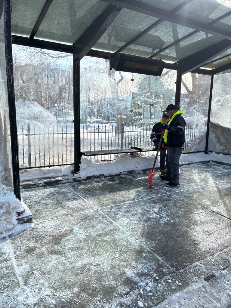 photo showing 2 workers that had recently cleared the snow out of a bus stop