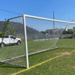 photo showing a soccer goal with wind turbines and a truck in the background
