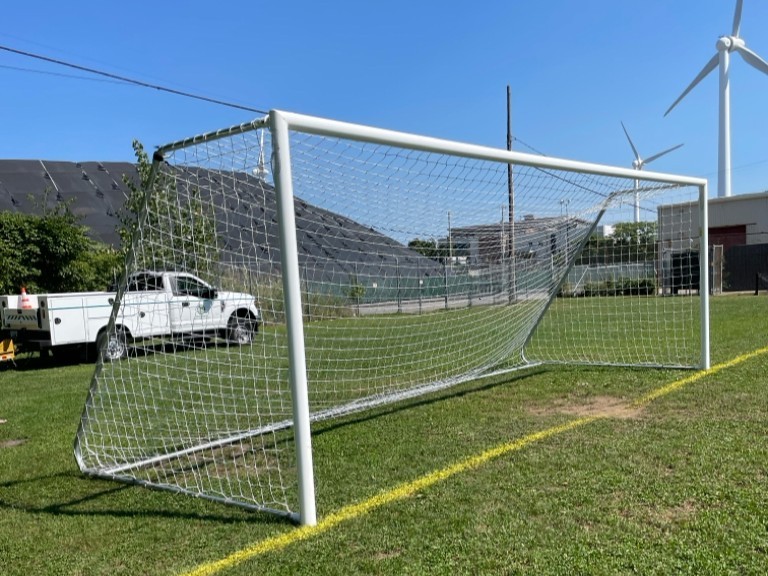 photo showing a soccer goal with wind turbines and a truck in the background