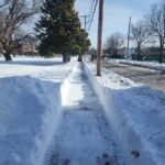 photo of a shoveled sidewalk with snow present everywhere in the photo