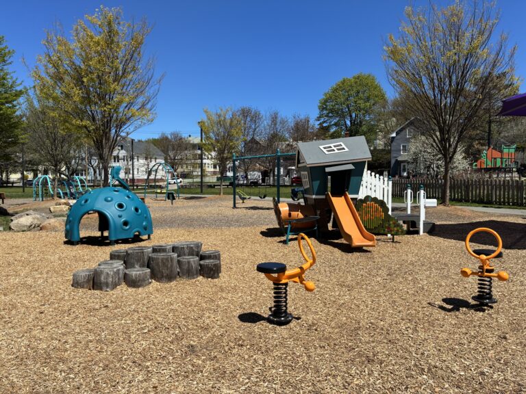 Father Lennon Park playground for ages 2-5 with spring rockers, balance feature, playhouse with slide, and climbing dome