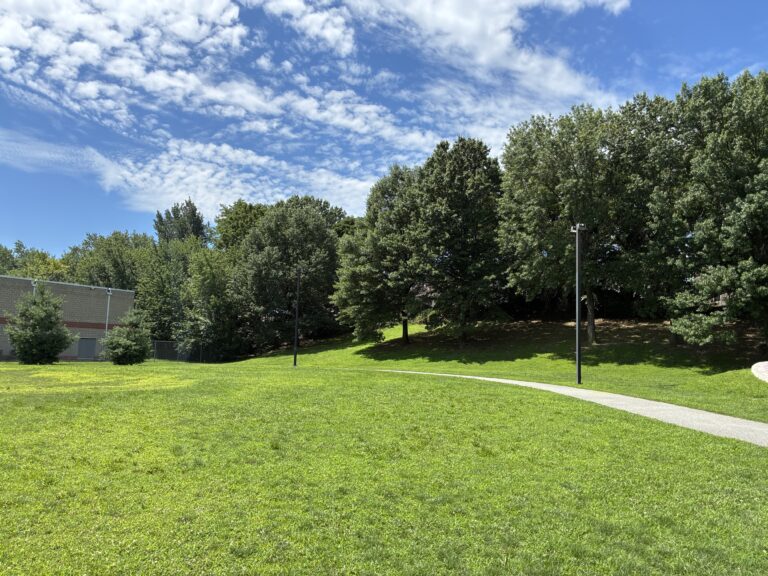 Father Lennon Park open field with lit paved walking path facing the Rec Center
