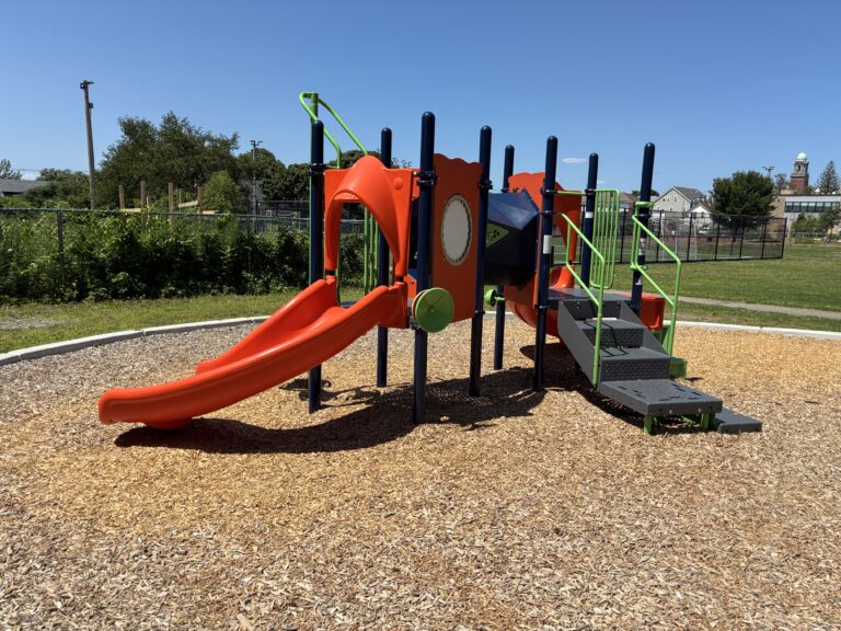 Joslin Park separate playground area for ages 2-5 with view of Olneyville skyline. That is a community garden behind the playground