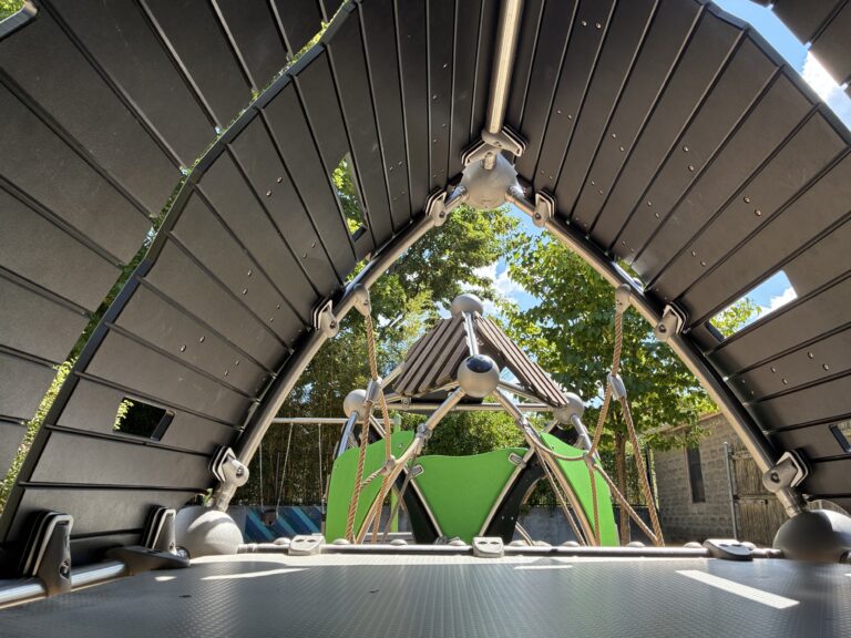 Morris Ave Park view inside the main play structure for ages 2-5. Looking from one covered pod to another across a cargo net bridge.