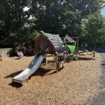 Morris Ave Park main play structure for ages 2-5 features a slide, activity panels, and various climbers including a cargo net