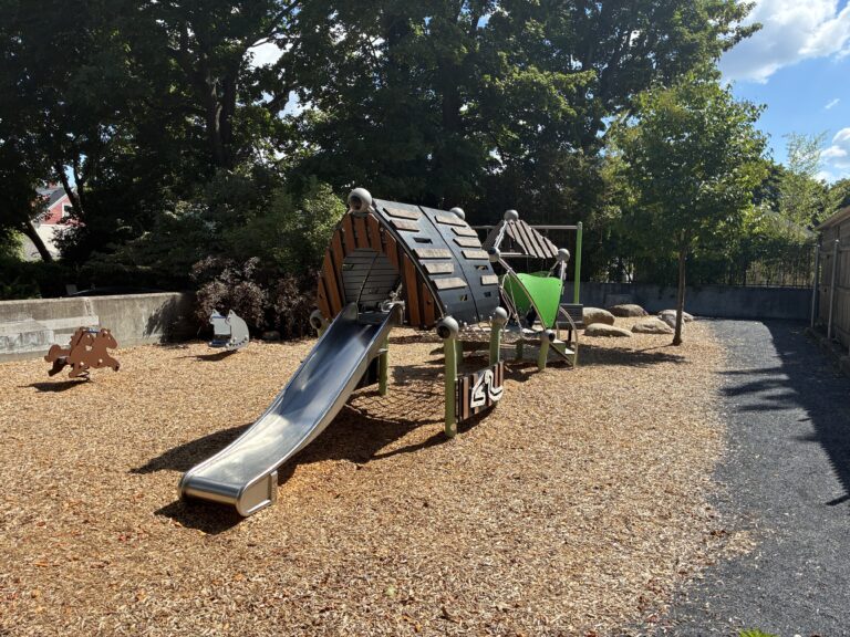 Morris Ave Park main play structure for ages 2-5 features a slide, activity panels, and various climbers including a cargo net
