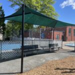 Pastore Park park benches with shade structure overlook the playground. Photo taken facing the waterpark