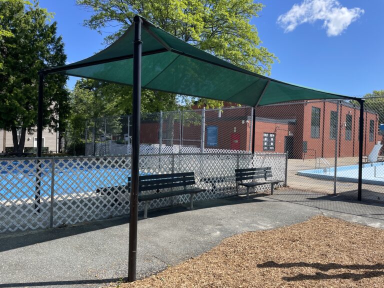 Pastore Park park benches with shade structure overlook the playground. Photo taken facing the waterpark