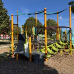 Richardson Park unique play structure for ages 5-12 features an obstacle course layout with various nets, ropes, belts, and traditional decks