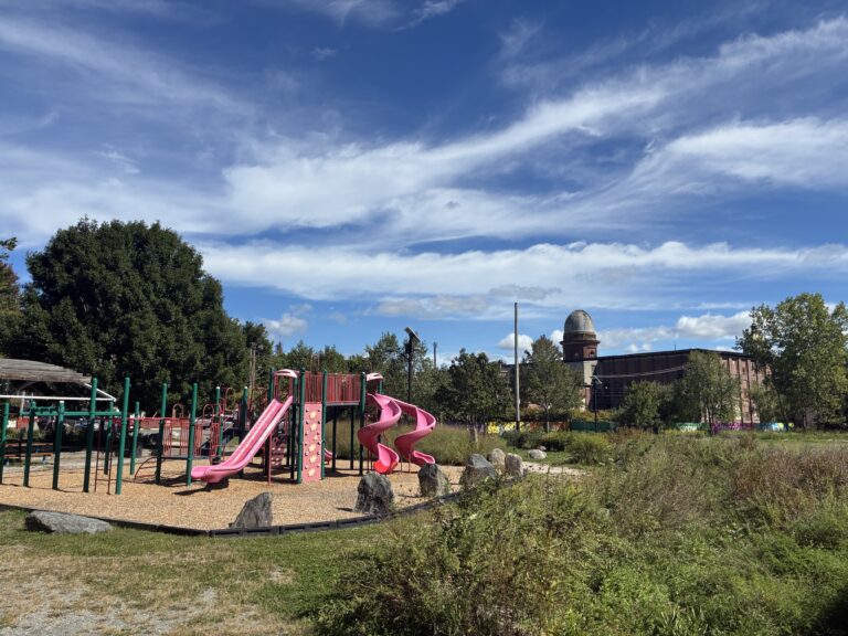 Riverside Park playground for ages 2-12 against the Olneyville skyline with one Atlantic Mills tower visible
